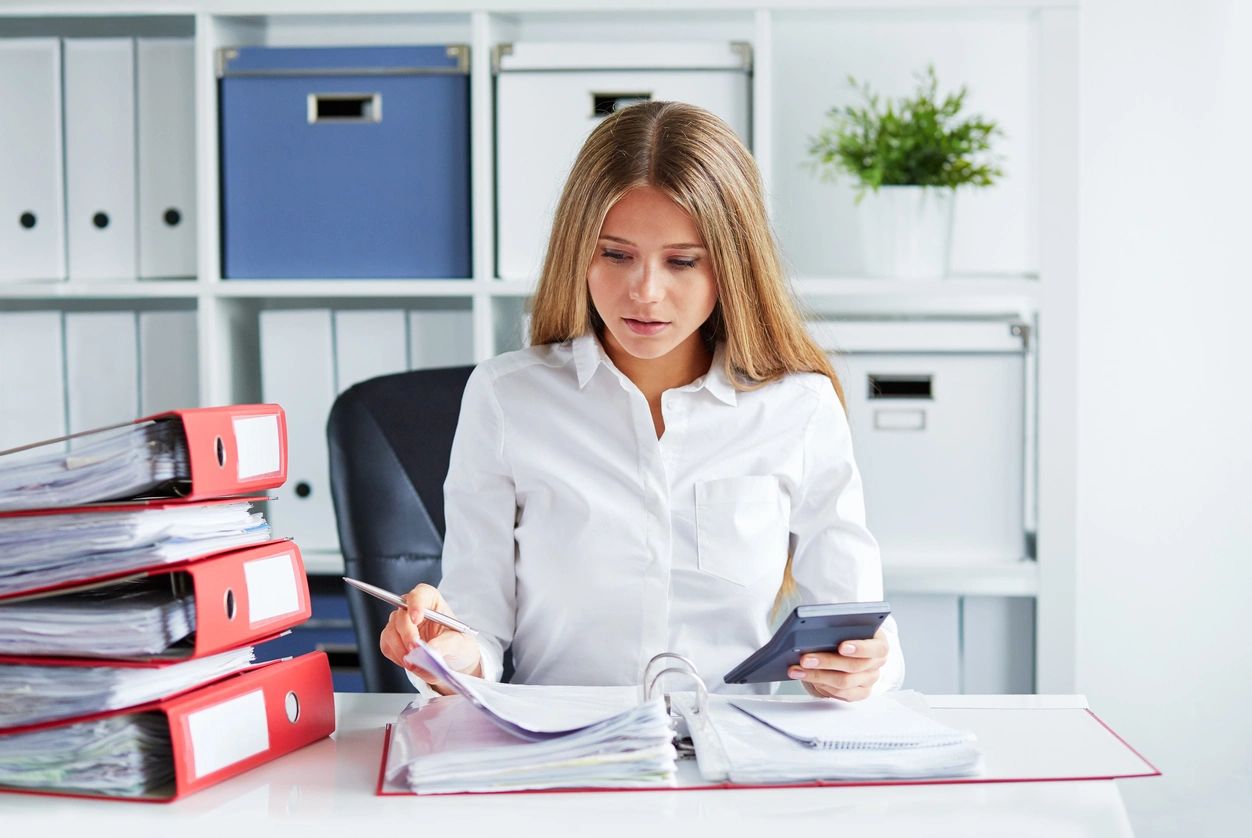 A woman sitting at her desk with papers and cell phone.